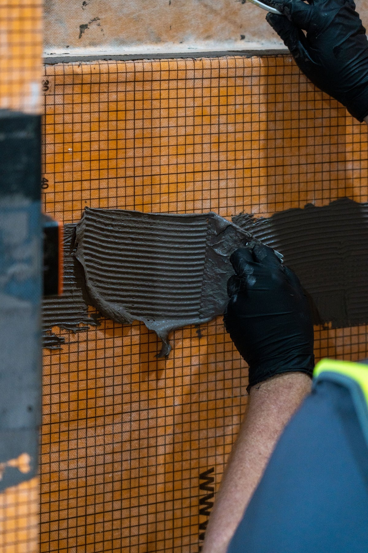 Applying tile adhesive to a Schlüter-DITRA uncoupling membrane during porcelain tile installation.