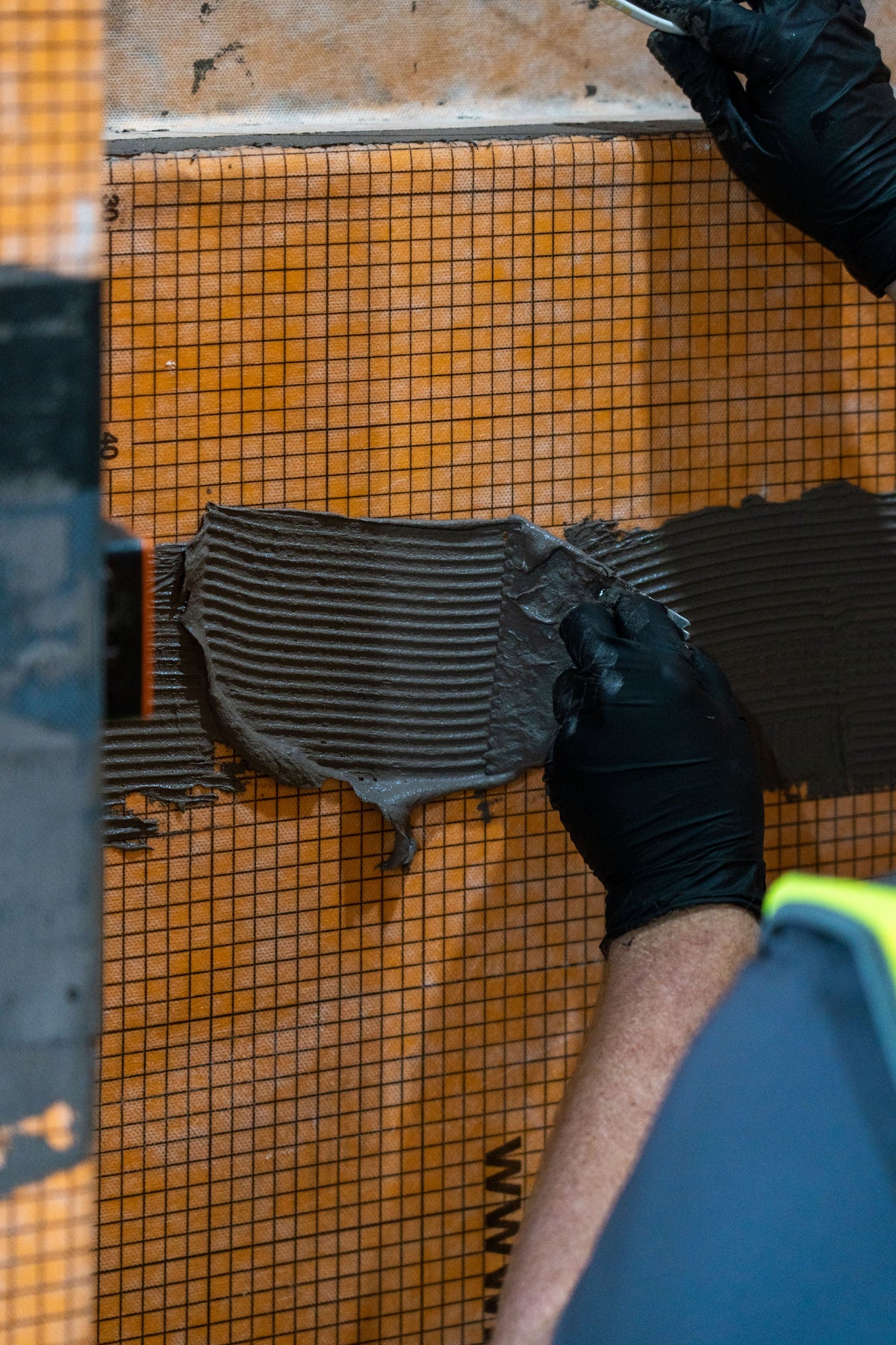 Applying tile adhesive to a Schlüter-DITRA uncoupling membrane during porcelain tile installation.
